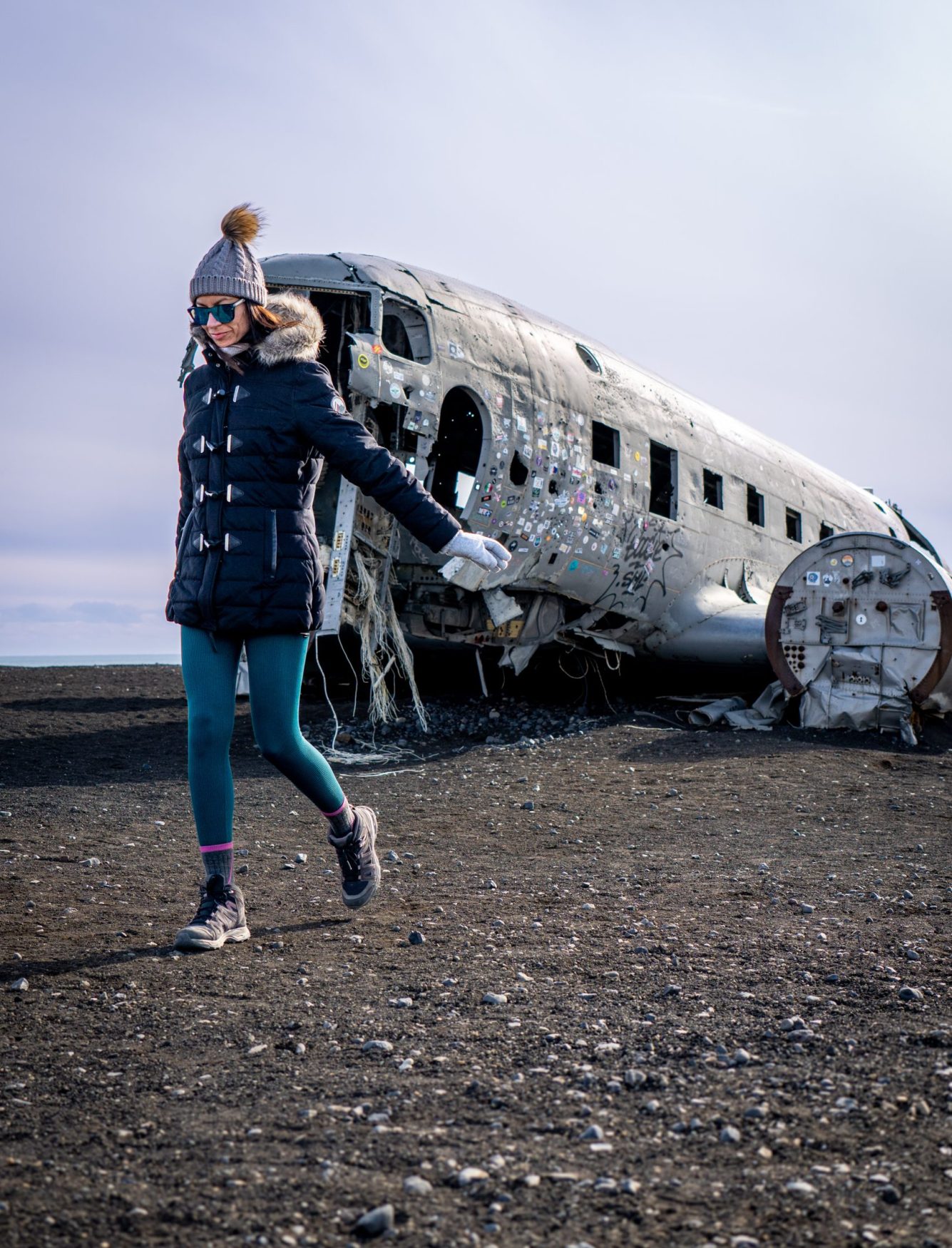 A vertical of a young woman walking against a damaged airplane